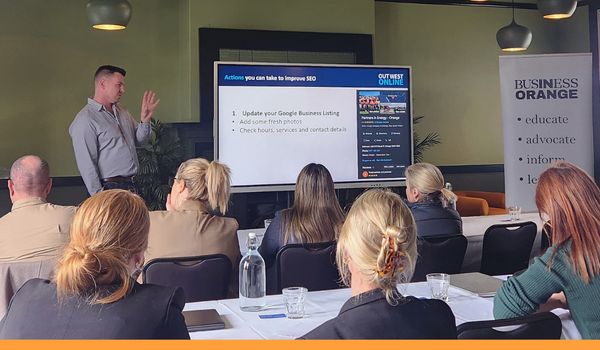 photo of a workshop from behind the audience. People are seated at desks watching a man at the front of the room present a slideshow.