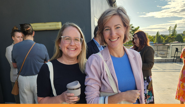 two blonde white women smiling at the camera with people networking on an outdoor patio behind them.